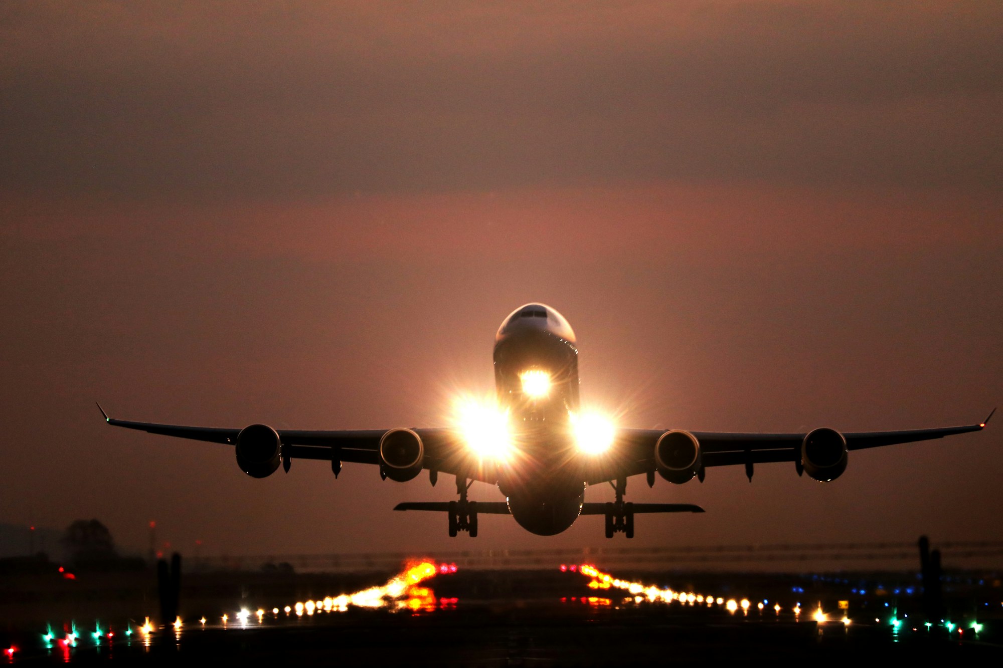 Wide-body airliner taking off at dusk over lit runway lights